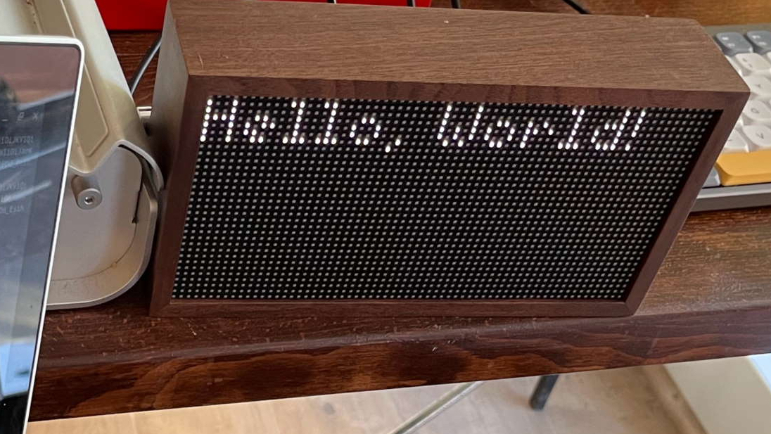 Tidbyt box displaying "Hello World!" next to a Chromebook terminal